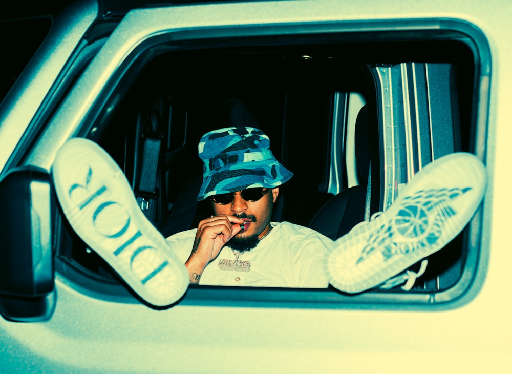 man in white and black jacket and blue cap sitting on car