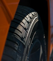 Close-up of a heavy-duty tire tread pressed into gritty asphalt, lit by electric orange light.