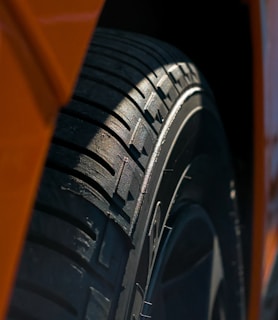 Close-up of a heavy-duty tire tread pressed into gritty asphalt, lit by electric orange light.