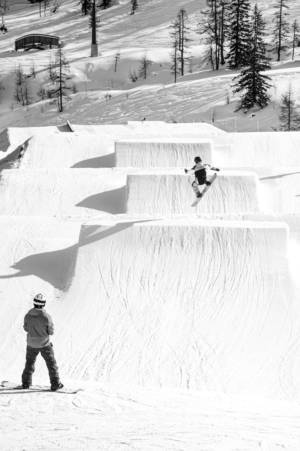 Foto en escala de grises de hombre con chaqueta y pantalones caminando en un campo cubierto de nieve