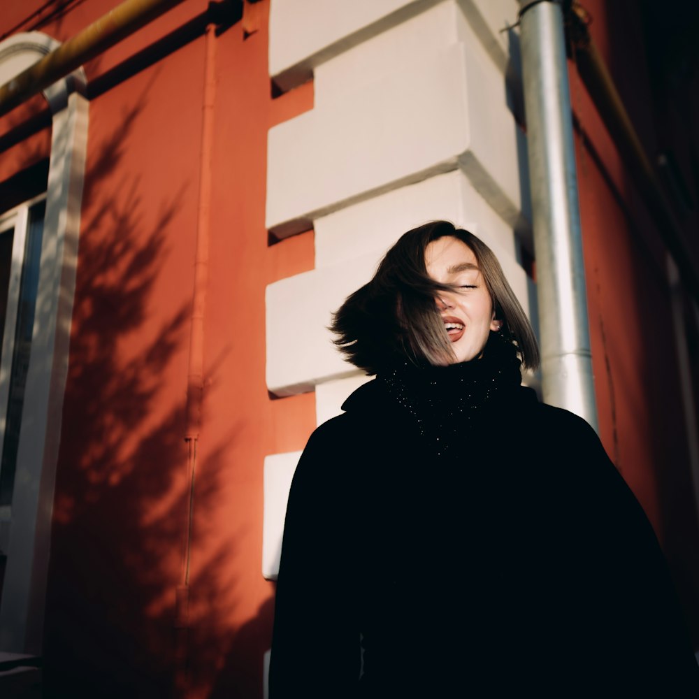 woman in black coat standing near orange wall