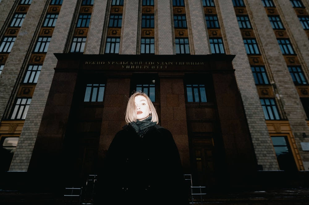 woman in black coat standing in front of brown building