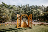 Sunlit outdoor wedding ceremony with floral arch and guests seated on wooden benches.