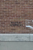 A red brick wall with the words 'MATIÈRE ÉPHÉMÈRE' stenciled in black paint. The lower section of the image shows a concrete base with some weathered texture.