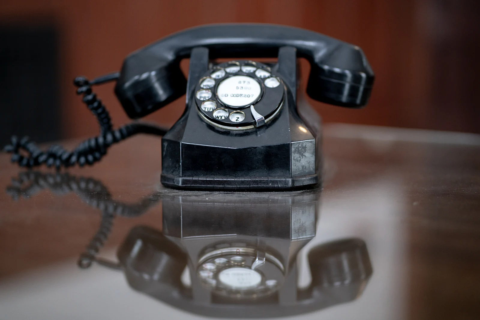 A black rotary desk telephone on a dark reflective desk.
