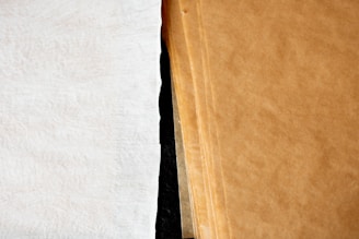 A close-up view of a stack of brown paper sheets next to a single white textured sheet, showcasing the contrast between the two surfaces.