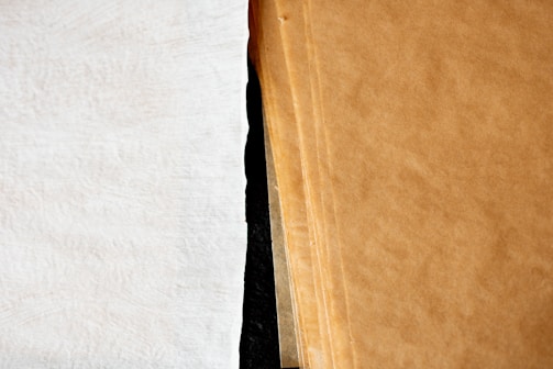 A close-up view of a stack of brown paper sheets next to a single white textured sheet, showcasing the contrast between the two surfaces.