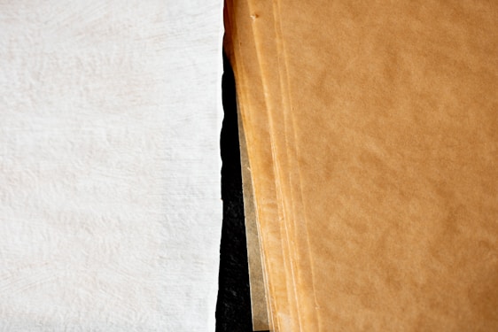 A close-up view of a stack of brown paper sheets next to a single white textured sheet, showcasing the contrast between the two surfaces.