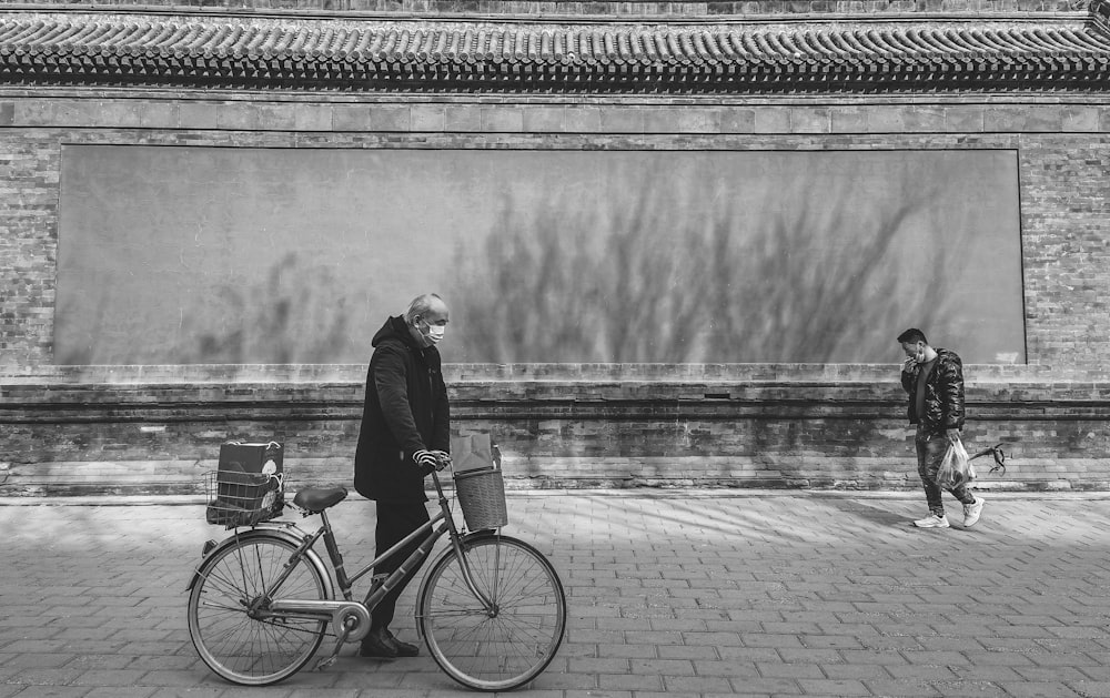 grayscale photo of woman standing beside bicycle near body of water