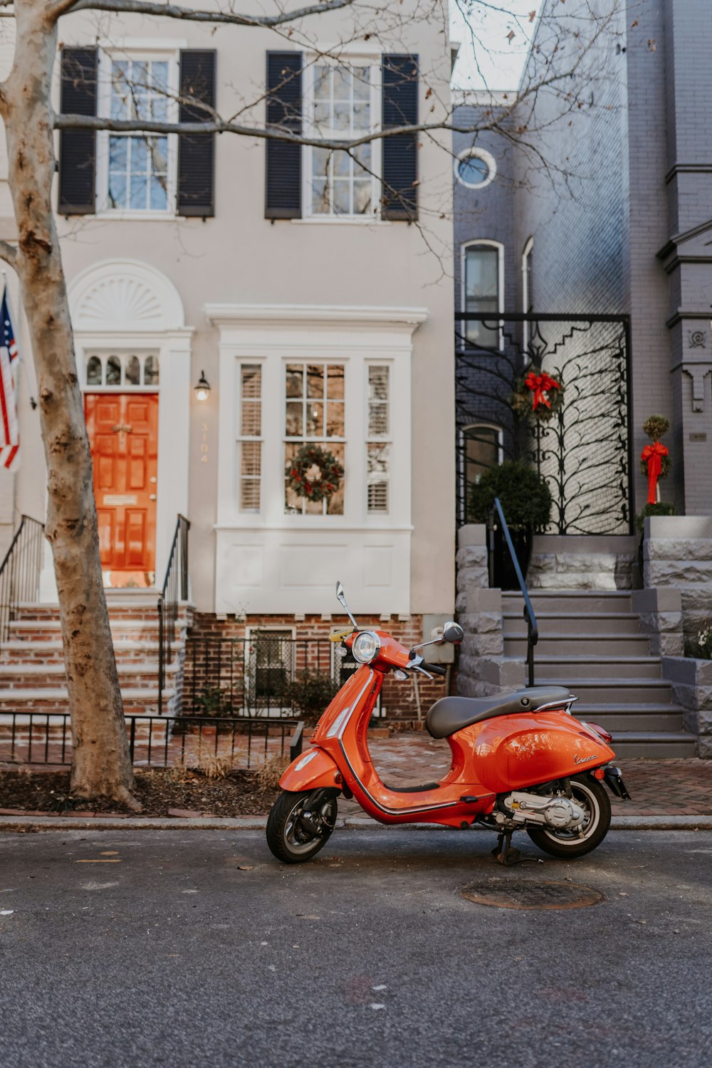 昼間、白いコンクリートの建物の脇に停車した赤と黒のモータースクーター