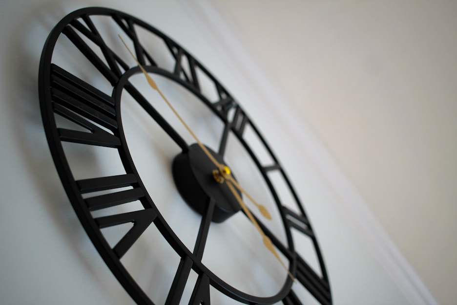 A sleek modern wall clock in black and gold hanging on a beige wall.