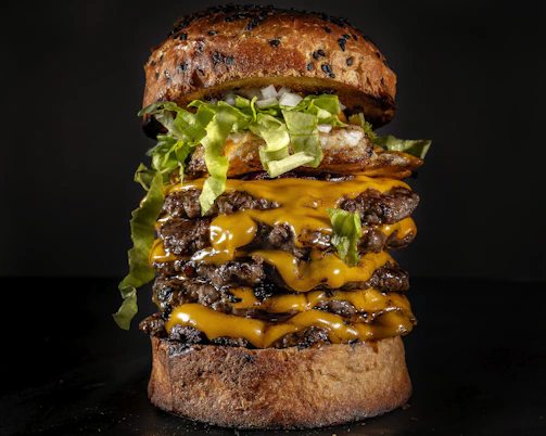 Stacked cheeseburger with melted cheese, fresh lettuce, and tomato on a toasted bun.