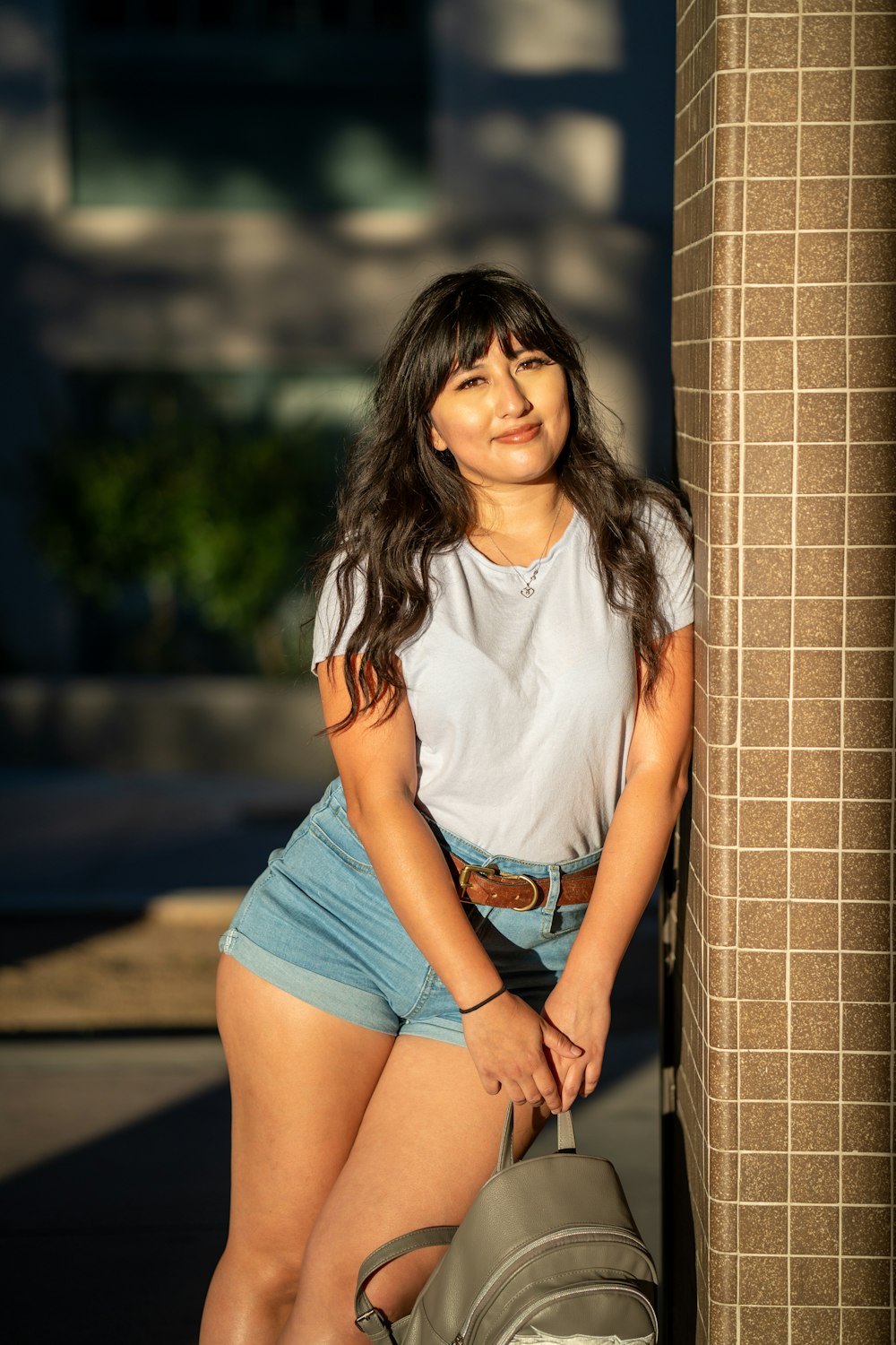 woman in white crew neck t-shirt and blue denim shorts leaning on brown brick wall