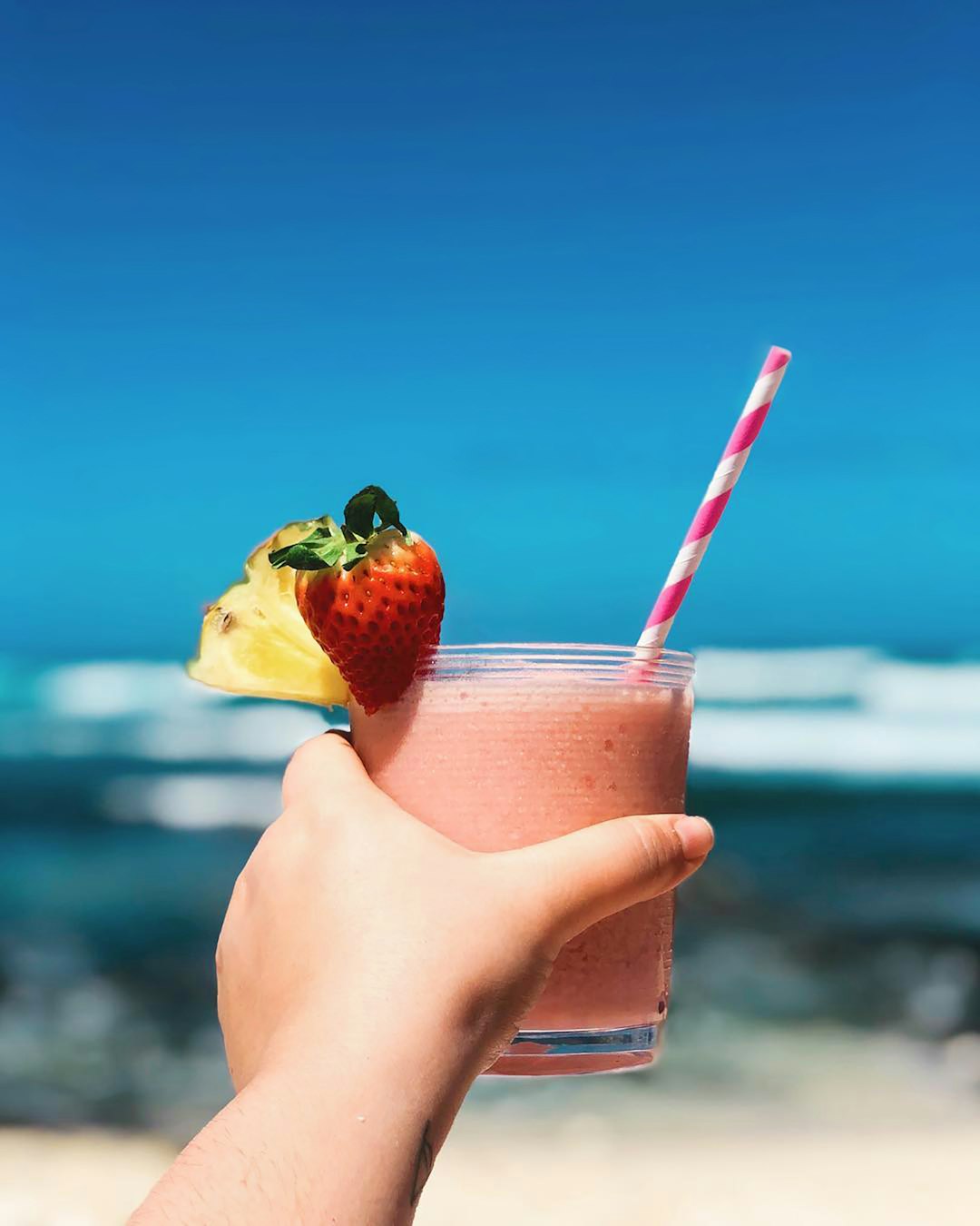 A hand holding a frozen alcoholic drink called a lava flow on the beach in Hawaii.