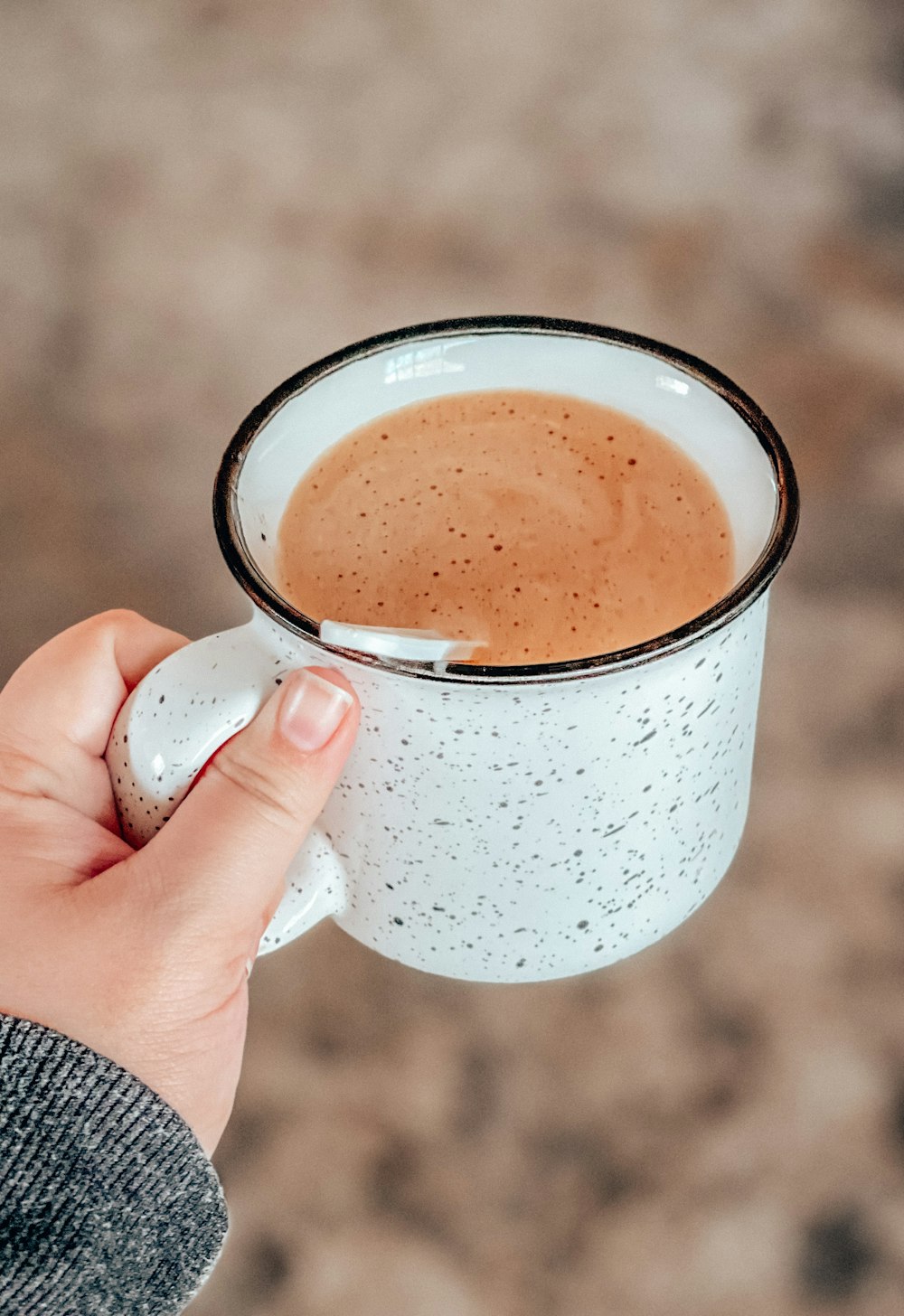 Persona sosteniendo una taza de cerámica blanca con líquido marrón