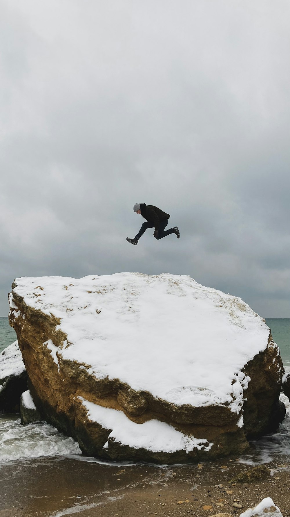 man in black jacket and pants jumping on white rock