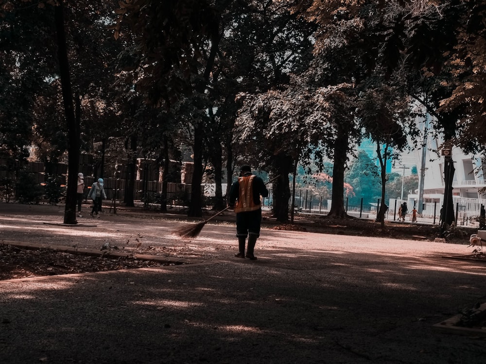 Donna in cappotto marrone che cammina sul sentiero circondato da alberi durante il giorno