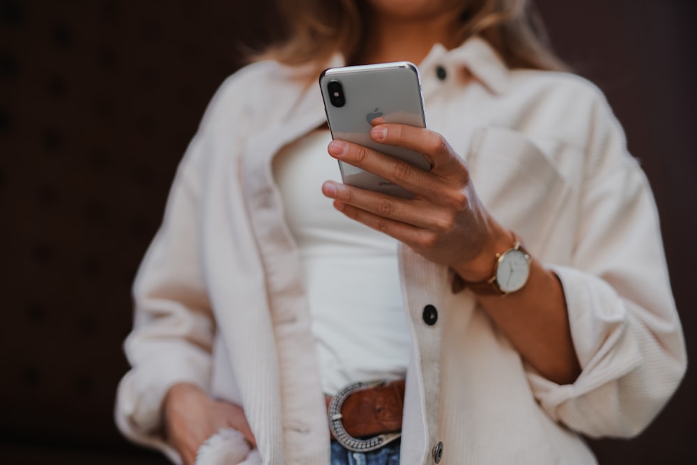 Femme en manteau blanc tenant un iPhone 6 argenté