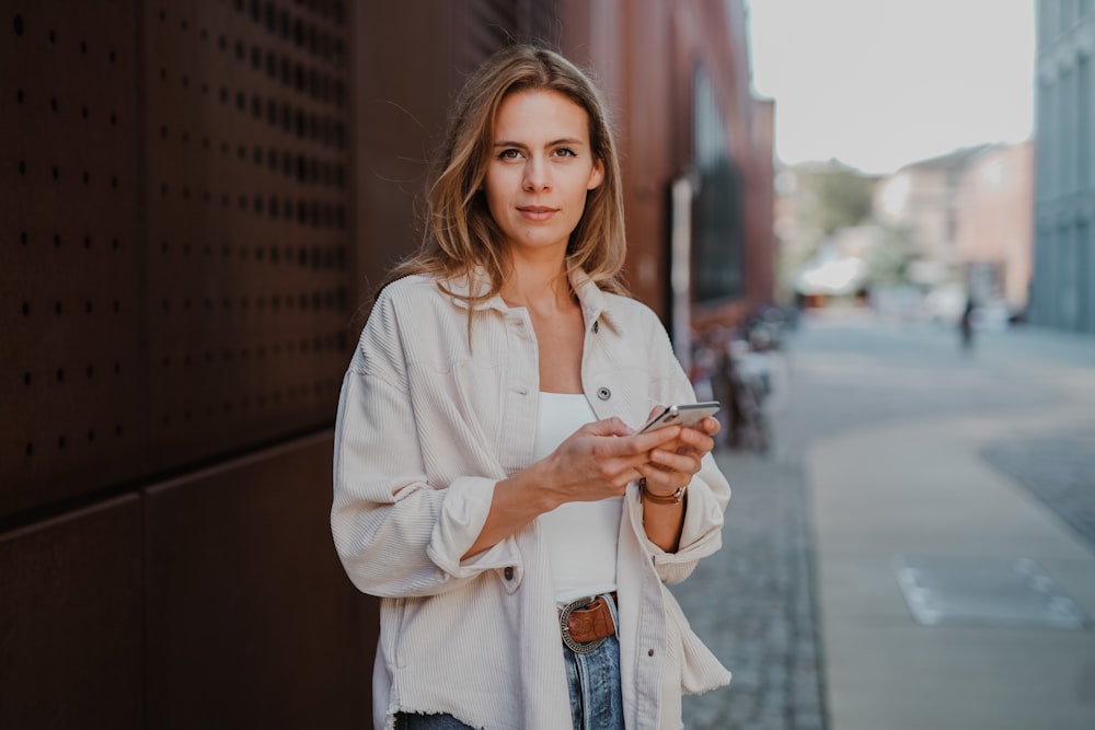 femme en blanc boutonnage jusqu’à chemise à manches longues tenant un smartphone blanc