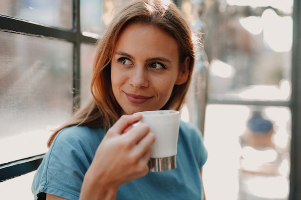 Smiling woman enjoying a cup of coffee by a sunny window.