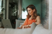 A smiling woman working on her laptop in a cozy home office, representing online business success.