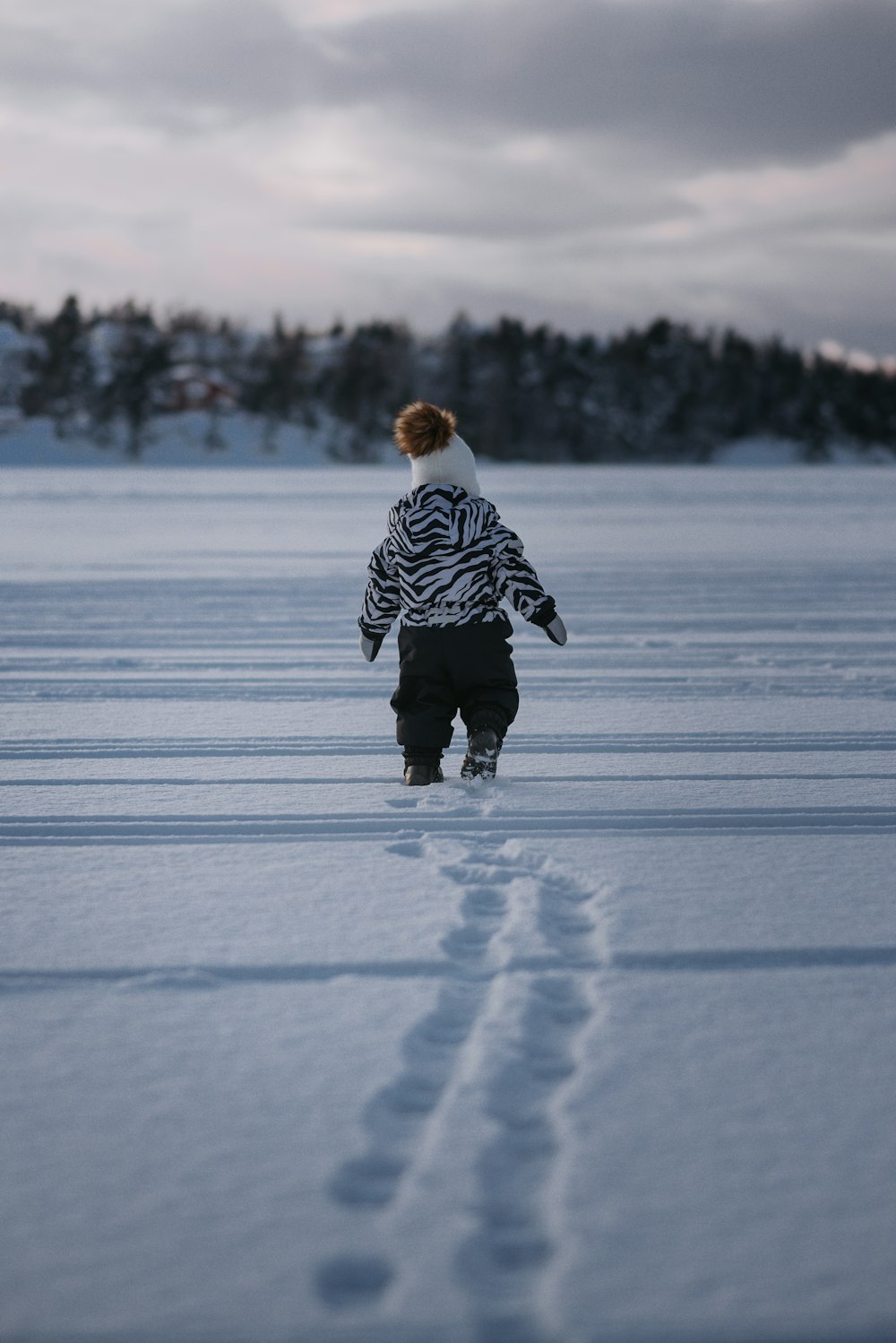 昼間、雪に覆われた地面を歩く黒と白の縞模様のジャケットを着た子供