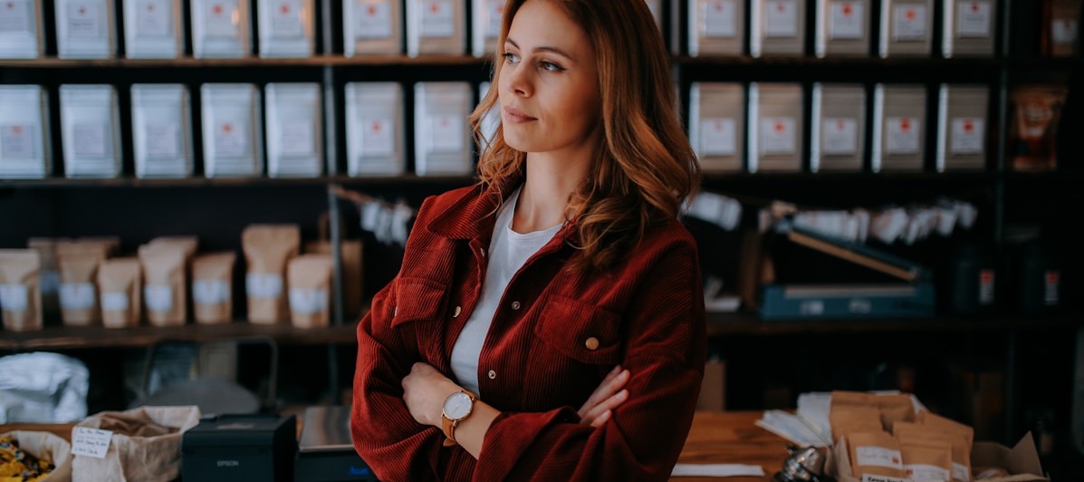 woman in brown jacket standing near black computer monitor