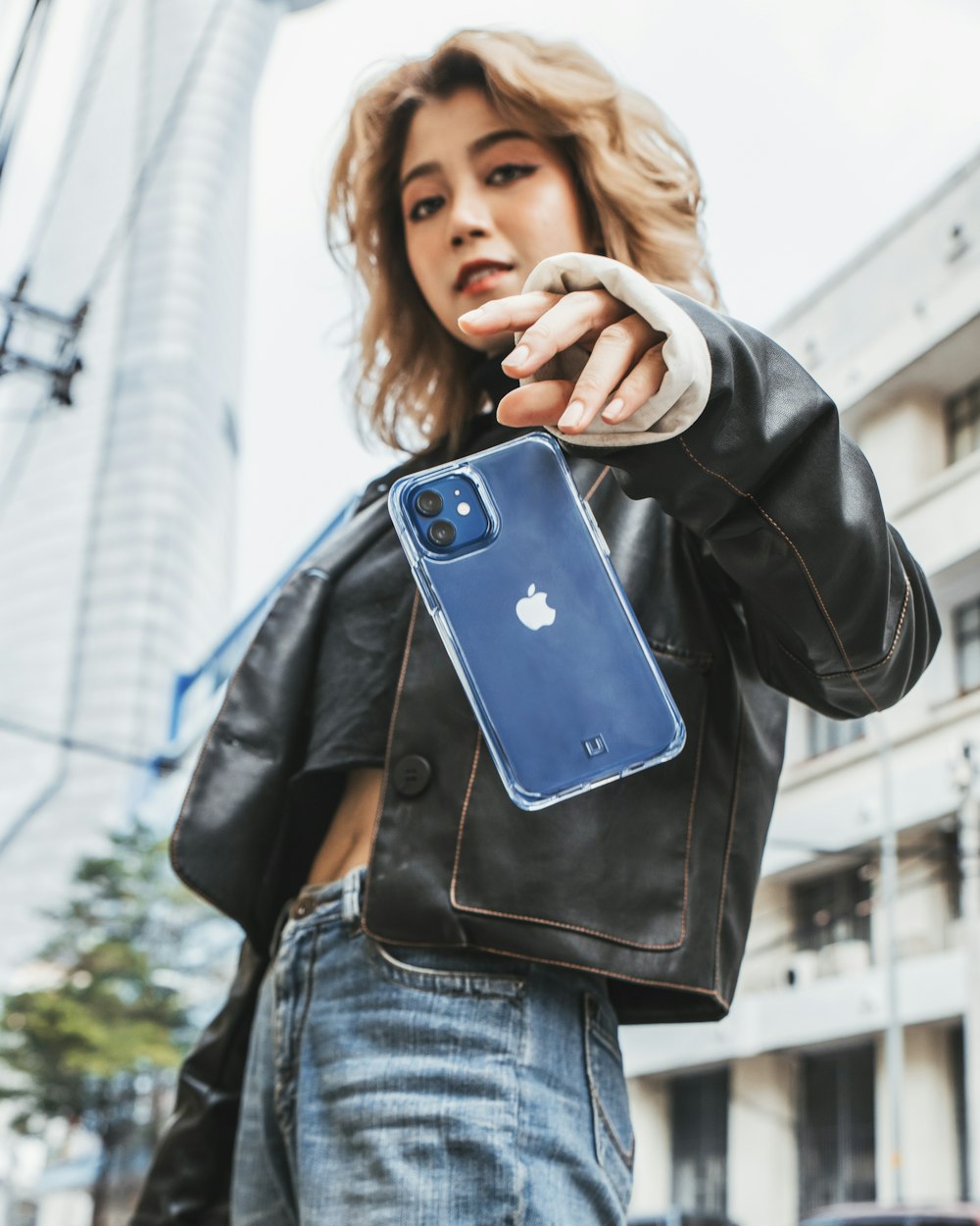 mulher na jaqueta de couro preta que segura o caso azul do iphone