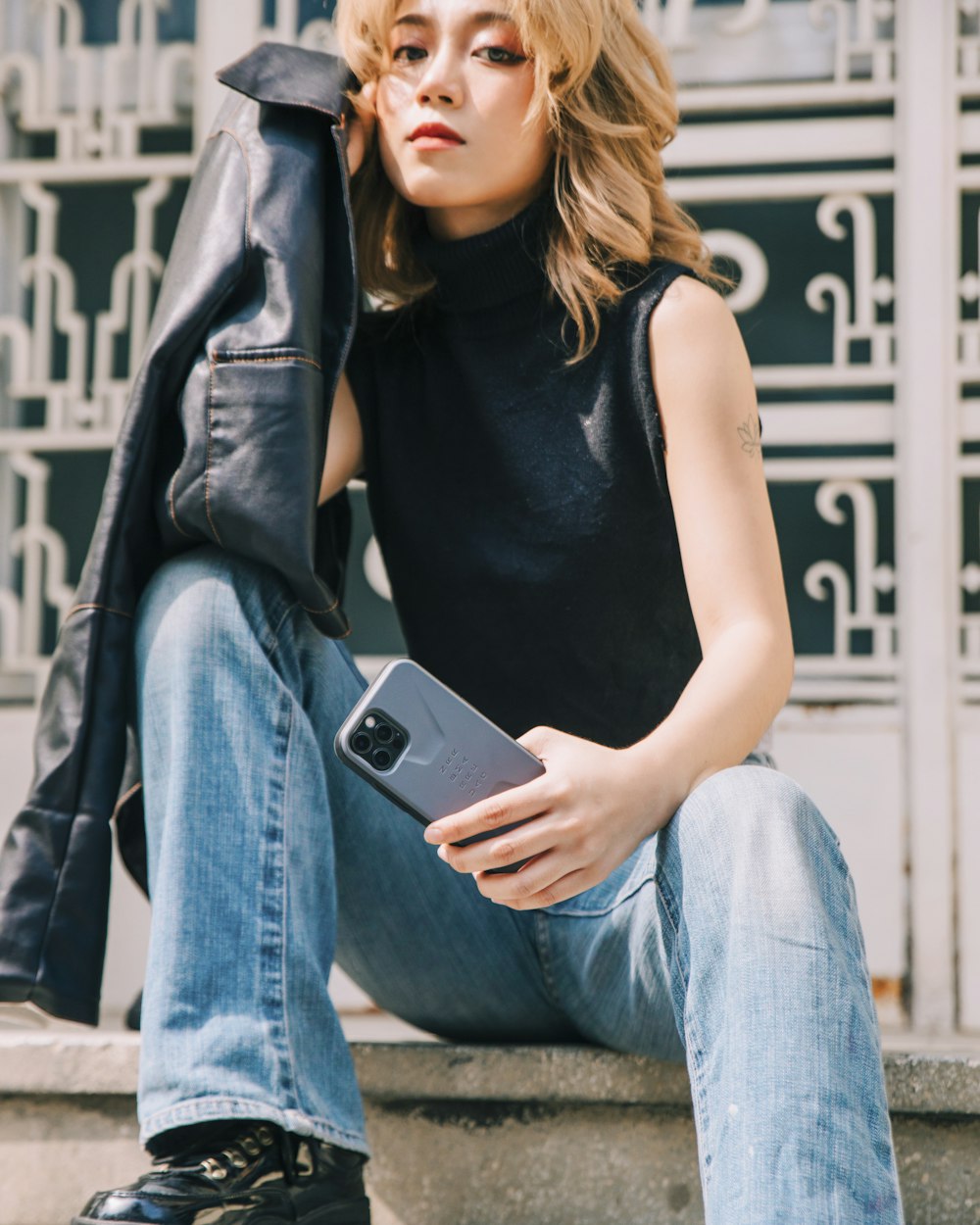 woman in black tank top and blue denim jeans holding black smartphone