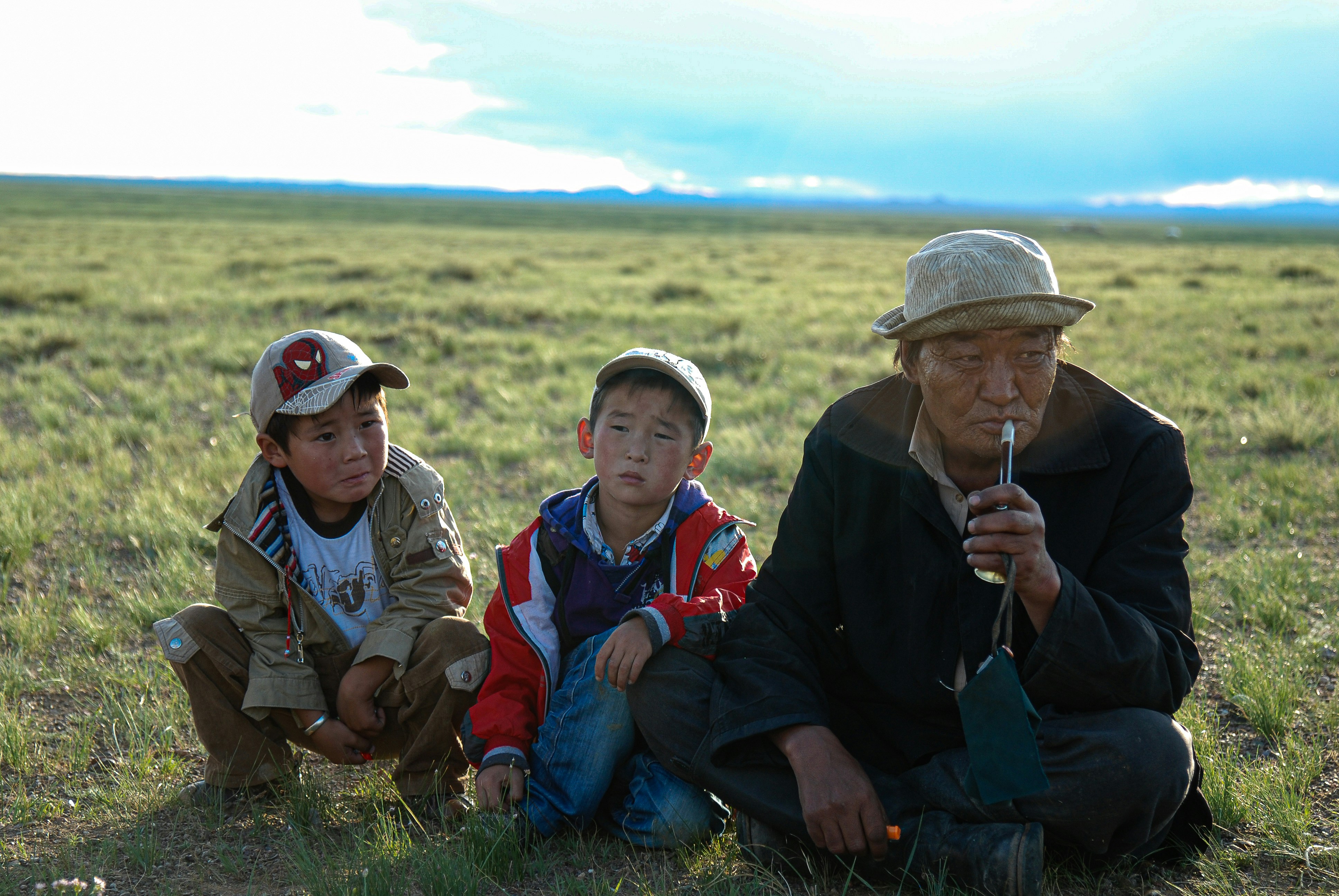 2 boys sitting on green grass field during daytime, Picture of a grandpa with his 3 kids, a classic Mongolian nomadic family.