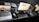 A neatly arranged workspace featuring three computer screens, including a MacBook, an iMac, and a second monitor. On the desk, there's a pair of headphones, a mouse, keyboards, a notepad, and other office items. In the background, two Mac Mini units and other electronic accessories are visible.