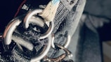 A close-up view of heavy-duty metal rings and thick, durable fabric straps, likely part of a harness or industrial equipment. The lighting creates a stark contrast, highlighting the textures and metallic surfaces.