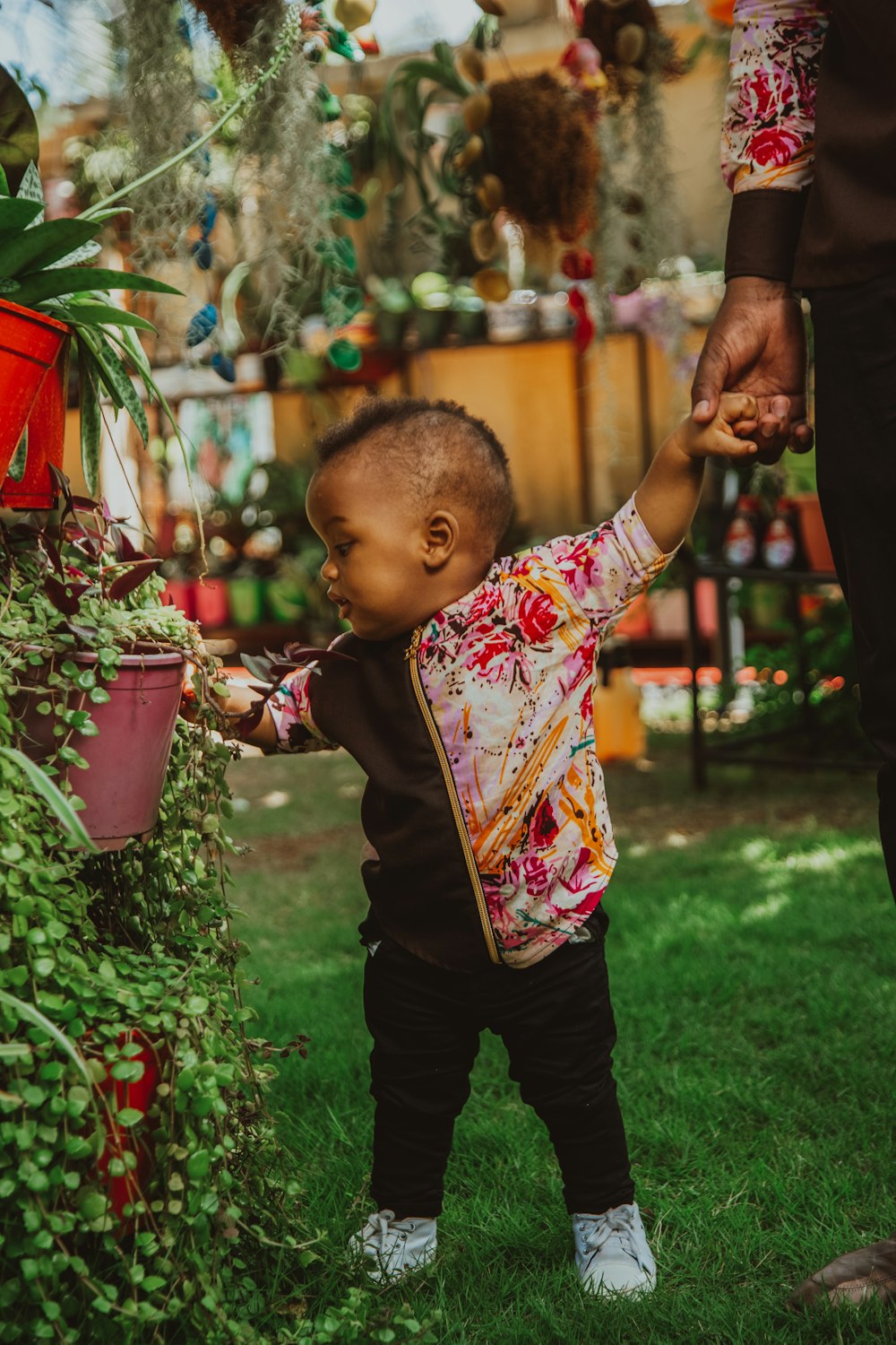 boy in red and white floral shirt and black pants standing on green grass field during