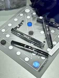 A board game layout featuring a combination of black and white circular pieces distributed across a translucent surface with geometric lines. The space includes several clear acrylic tubes with inscriptions, and a labeled section that reads 'AMORE PACIFIC'. A few irregularly shaped dark and light objects are placed alongside the game setup.