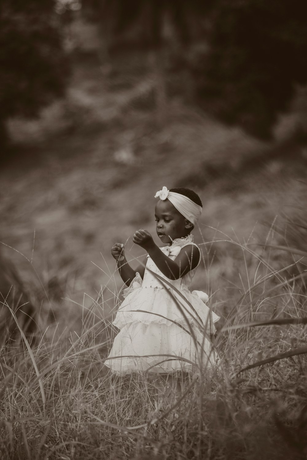 Photo en niveaux de gris d’une femme en robe blanche debout sur un champ d’herbe