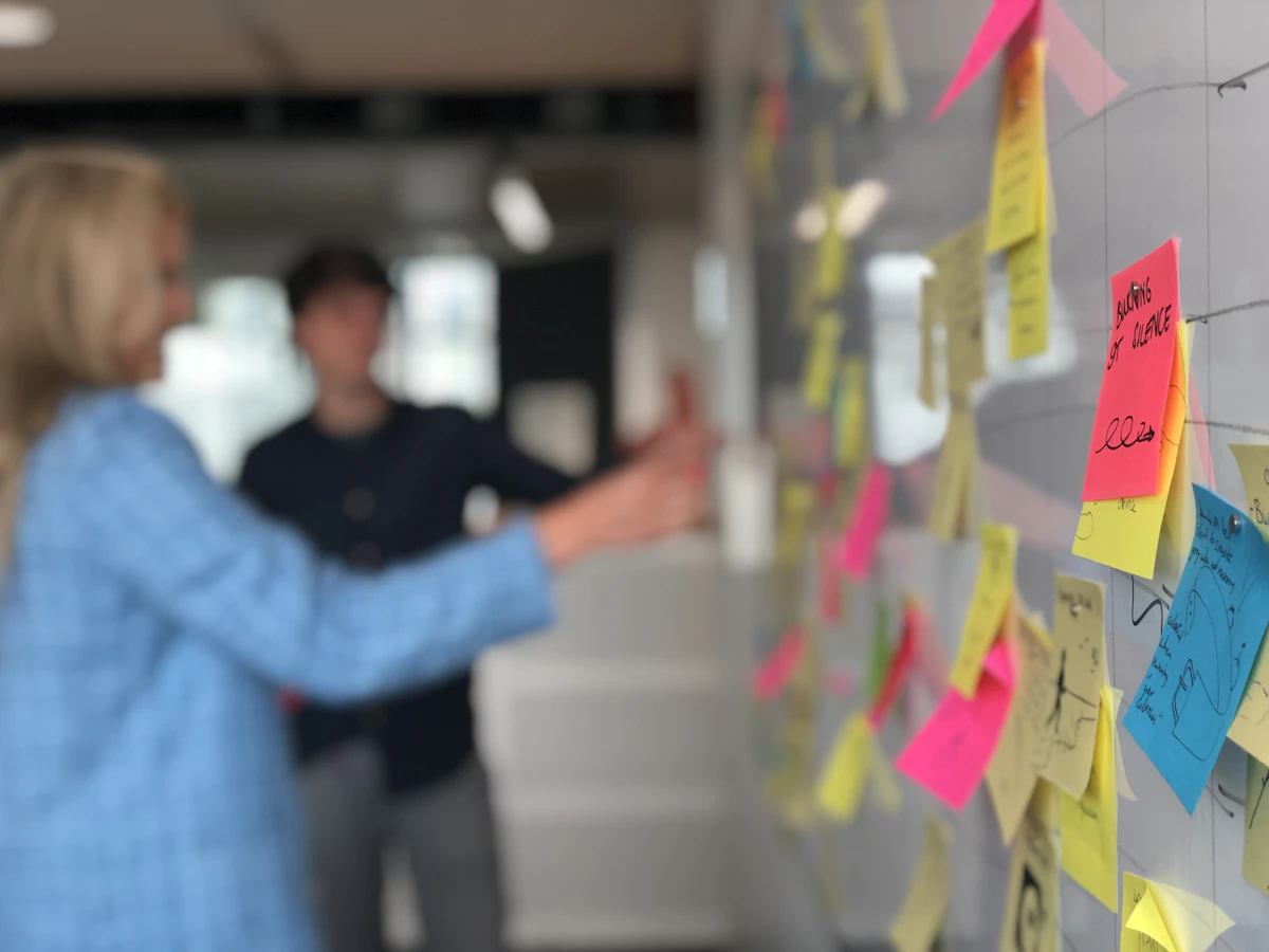 Two people arguing a point in front of a glass wall of handwritten notes, one with a hand raised