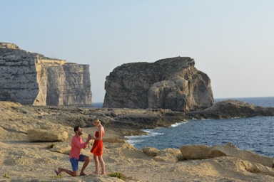 the knee,how to photograph wedding proposal at sunset in malta; woman in red tank top standing on seashore during daytime