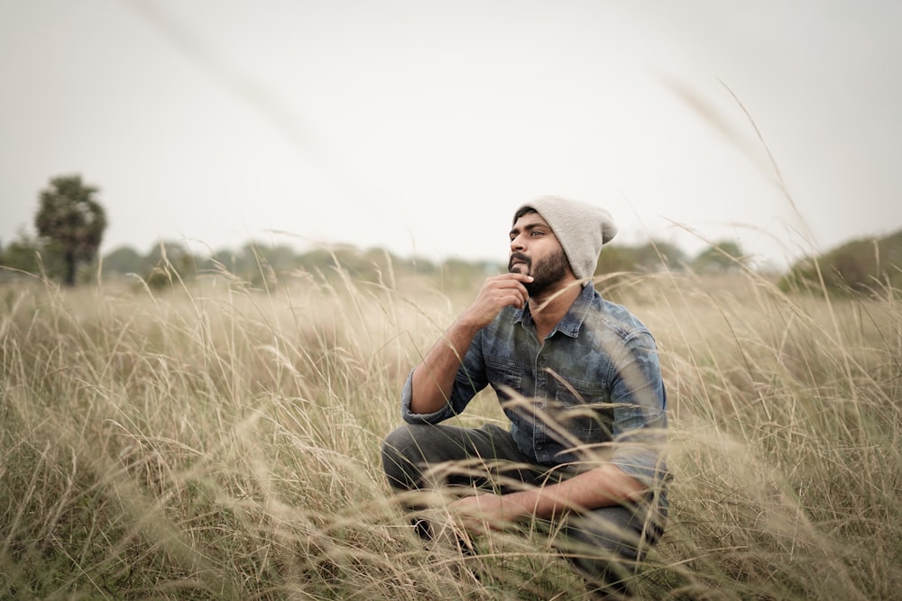 man in blue denim jacket and gray hat sitting on brown grass field