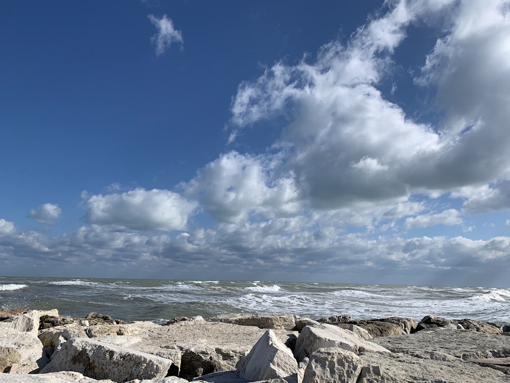 gray rocks on seashore under blue sky and white clouds during daytime