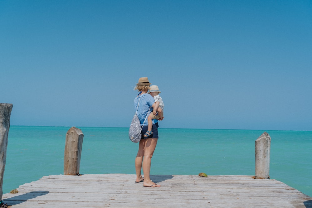 woman in blue denim shorts and brown sun hat standing on brown wooden dock during daytime