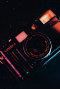 A vintage camera with prominent branding and lens details is captured in a low-light setting, emphasizing the metallic texture and intricate design. The camera's body reflects warm and cool lighting, creating a striking contrast.