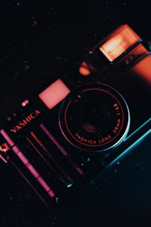 A vintage camera with prominent branding and lens details is captured in a low-light setting, emphasizing the metallic texture and intricate design. The camera's body reflects warm and cool lighting, creating a striking contrast.
