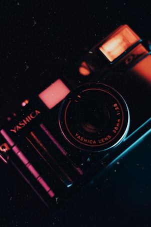 A vintage camera with prominent branding and lens details is captured in a low-light setting, emphasizing the metallic texture and intricate design. The camera's body reflects warm and cool lighting, creating a striking contrast.