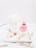 A white candle shaped like a female torso stands upright on a marble tray next to a pink, faceted perfume bottle. Gold jewelry, including a ring, earrings, and a necklace with a pendant, are also placed on the tray, which has a marbled pattern background.
