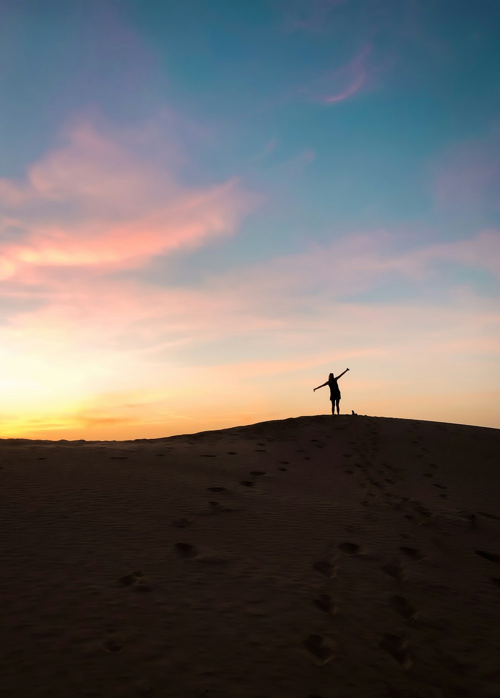 Silhouette einer Person, die während des Sonnenuntergangs auf braunem Sand steht