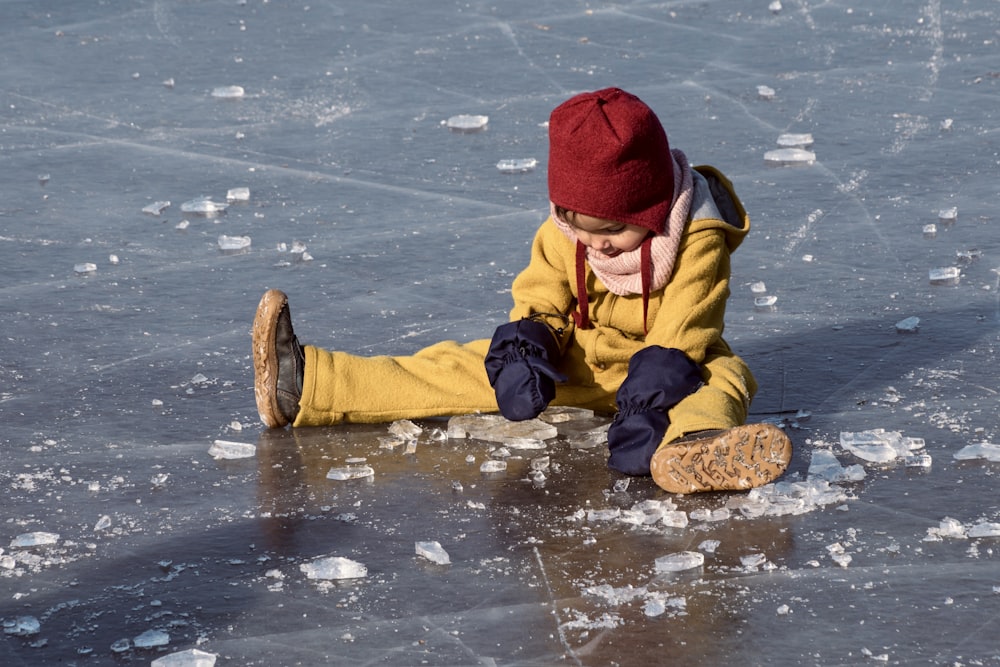 child in yellow jacket and red knit cap playing on water