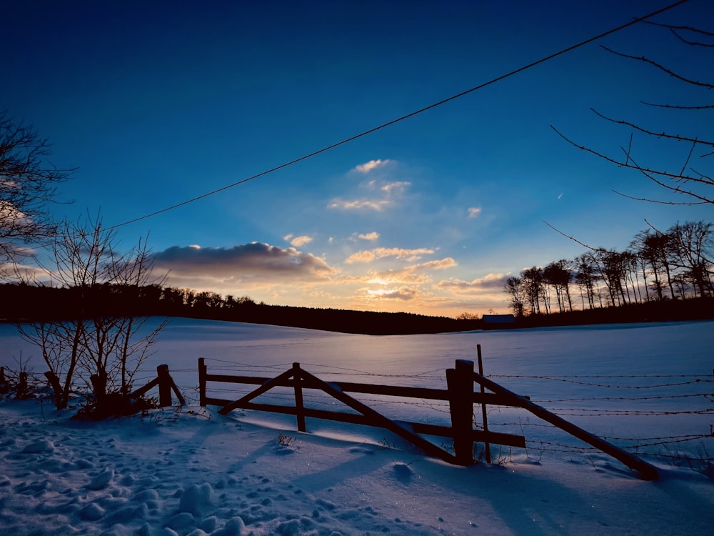 brown wooden fence on snow covered ground during sunset