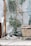 A calico cat is lounging on a cushion in a bright, sunlit space. The area is decorated with plants, a wooden ladder, and a wicker basket. There is a transparent plastic sheet in the background, adding a soft, filtered light to the scene.