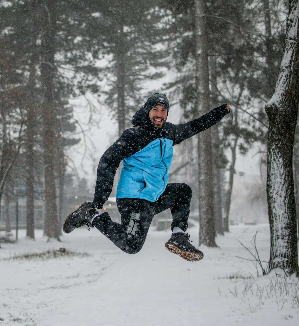 uomo in giacca blu e pantaloni neri seduto su terreno coperto di neve durante il giorno