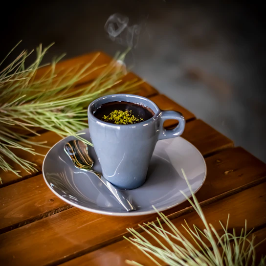 A serene cup of steaming herbal tea surrounded by fresh green botanicals on a wooden table.